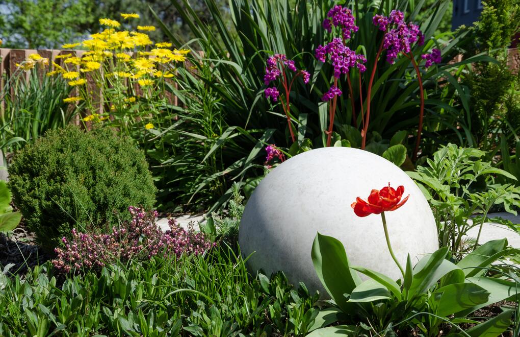Hladká betonová koule v rozkvetlé zahradě