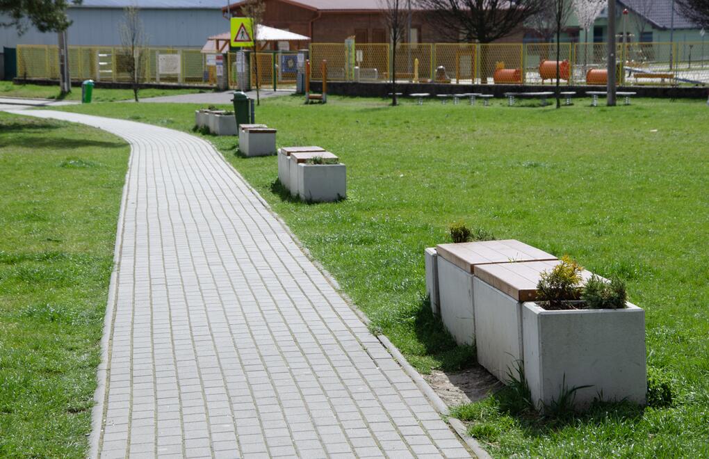 Betonové lavičky a květináče městského mobiliáře PREFACUBE na pěší promenádě u dětského hřiště